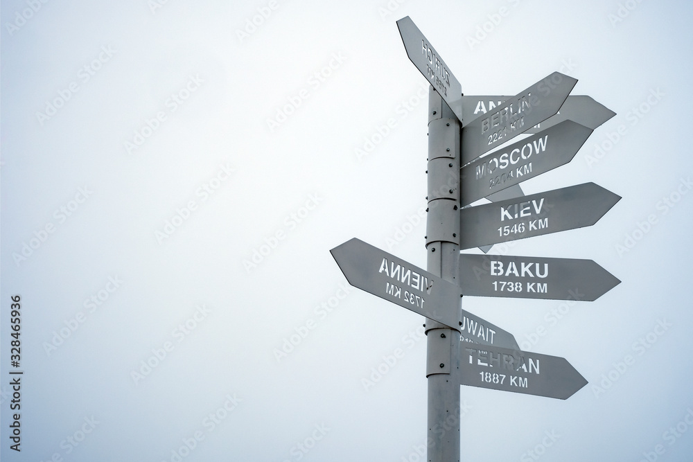 Gray direction sign pointing on capitals of countries on a gray foggy sky background. Tahtali mountain's peak, Turkey. Gray direction sign pointing on capitals of countries on a gray foggy sky background. Tahtali mountain's peak, Turkey.