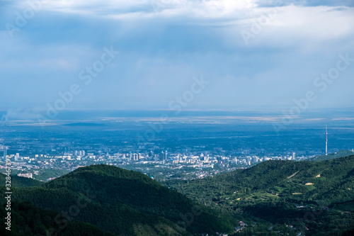 Beautiful view to Almaty city and foothills with storm clouds captured from mountains. Green almaty mountains foothills clouds in beautiful style on blue background.