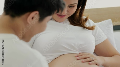 Tilting close up scene video of Asian couple. Man rubbed her stomach and felt that the baby kicked mother's belly. They are happy.