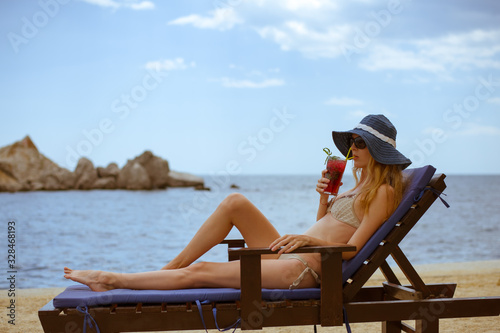 Beautiful slender young woman in a bikini swimsuit sunbathes and rests with cocktail in a glass © katafree