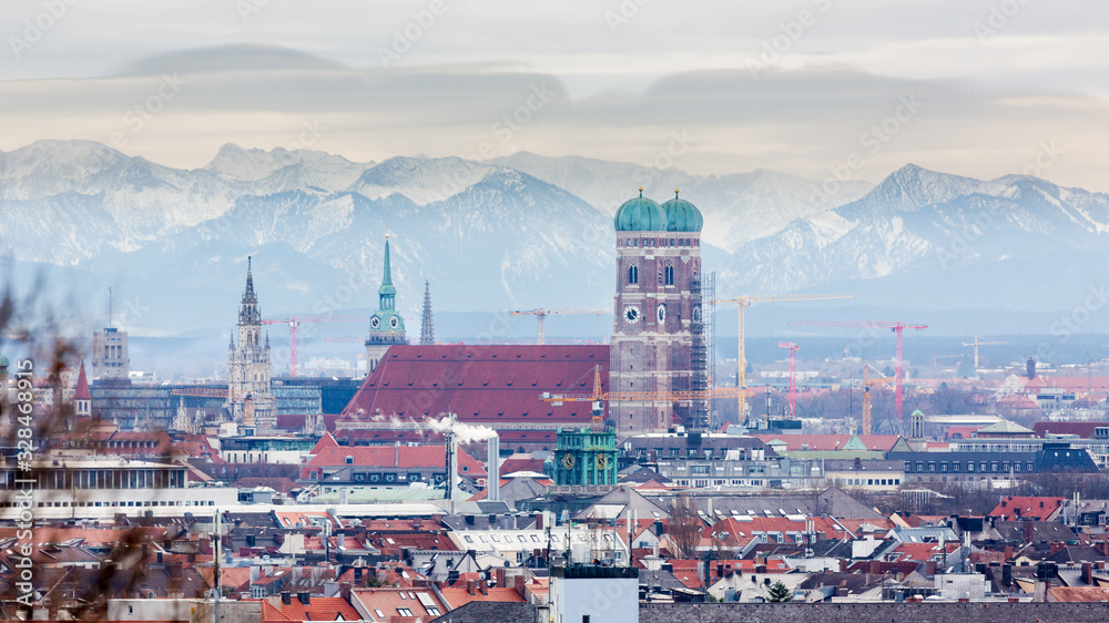 Munich, Bavaria / Germany - Feb 20, 2020: Frauenkirche with snow-capped alps (mountains) in the background. Symbol & landmark of the bavarian capital. Beautiful panorama captured during winter season. - obrazy, fototapety, plakaty 