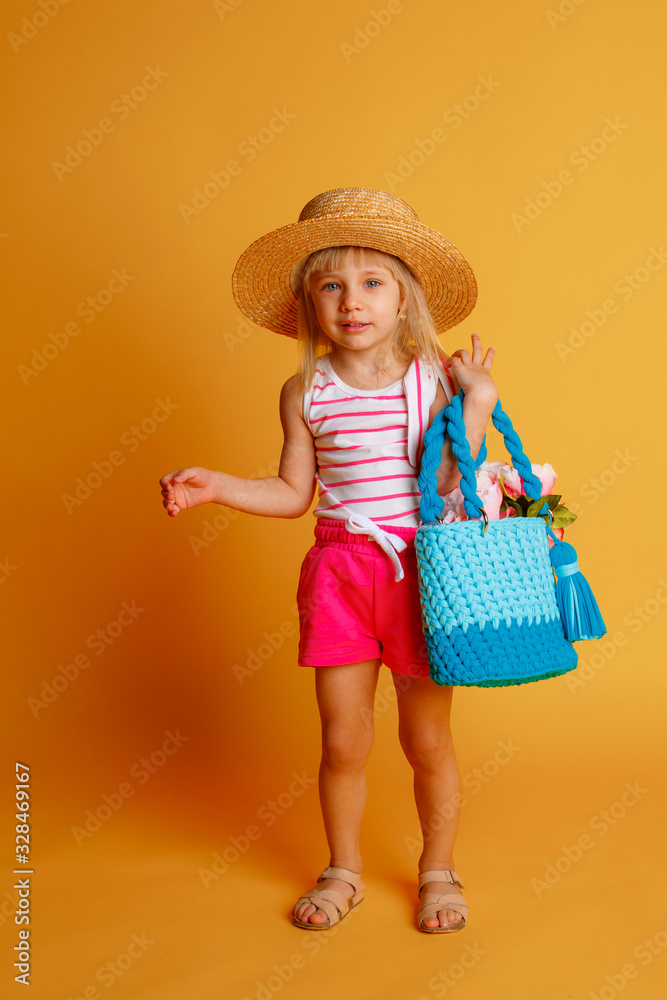 a little girl in summer clothes, a straw hat and a handbag with flowers on a yellow background. The concept of summer vacation