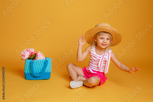 a little girl in summer clothes, a straw hat and a handbag with flowers on a yellow background. The concept of summer vacation