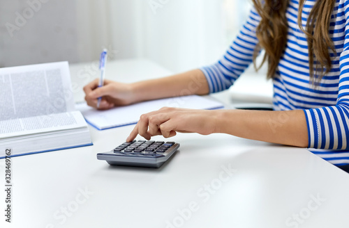 education, school and knowledge concept - close up of student girl counting on calculator and writing to notebook at home