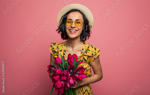 The portrait of a happy excited gorgeous young woman in stylish wear is posing with a freshness bunch of tulips. Mothers day. Women s holidays. Springtime.