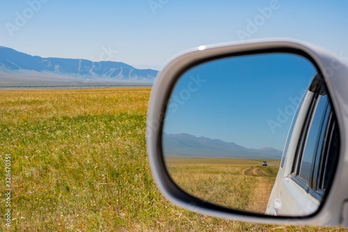 Car side mirror with gravel road and mountains background. Travel lifestyle. Car tourism.