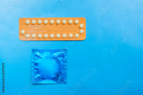 Contraception pills and condom on blue background. Male and female contraceptives concept. Bitrh control concept. photo