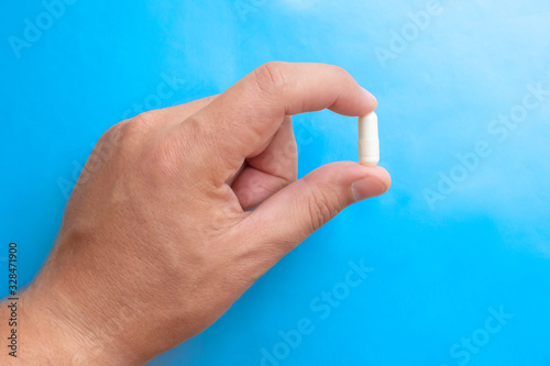 Hand holding white pill on blue background, great design for any purposes. Health care medical background. Medicine, healthcare concept. Pharmacy concept. Medicine pill.