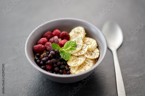 food and breakfast concept - oatmeal cereals in bowl with wild berries, banana and spoon on slate stone table