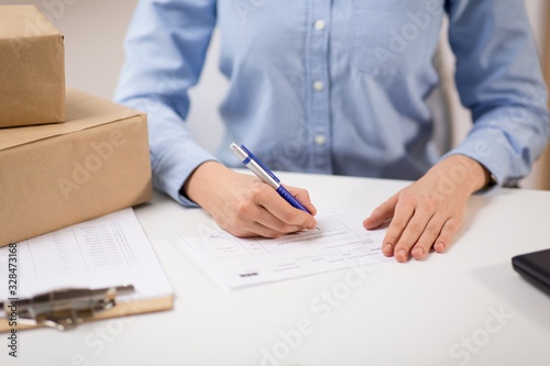 delivery, mail service, people and shipment concept - close up of woman filling postal form at office