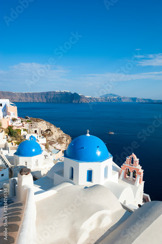 Whitewashed Greek church featuring bright blue dome and pink bell tower overlooking a Mediterranean blue caldera view in Santorini, Greece