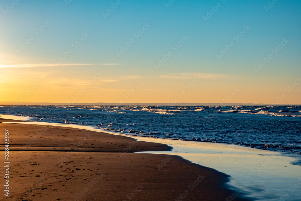 Obraz premium Wet sand on the coast at low tide wit clear blue sky and sea on a background.