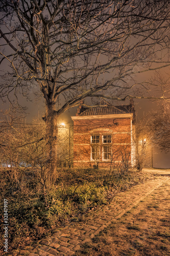 Foggy night scene small illuminated brick dike house