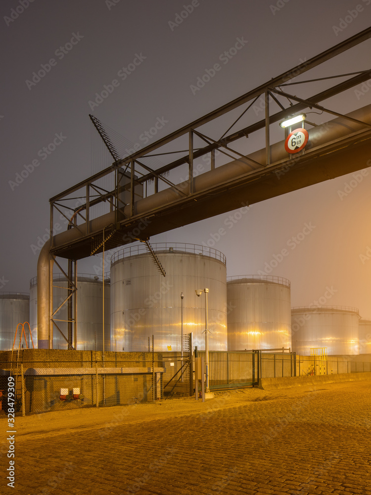 Night scene with large silo and pipeline overpass at petrochemical production plant, Port of Antwerp.