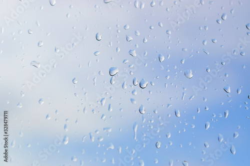 Abstract blurred of water drops or raindrops on the glass of window over blur sky used for background.