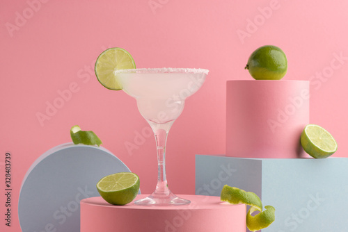 Glass of Margarita cocktail and fresh limes on pink background photo