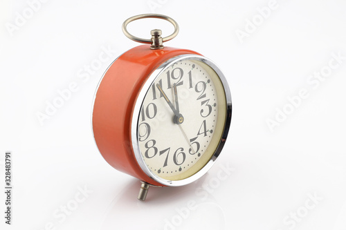 Old orange alarm clock separated on white background. Five minutes to twelve. Analog clock.