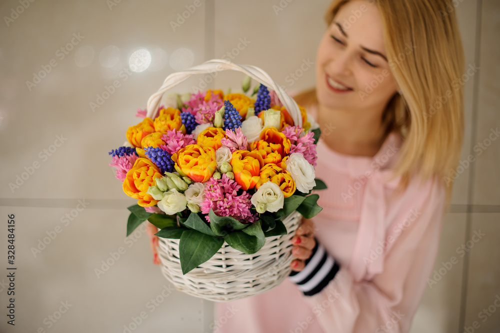 Woman holds in her hands a decorative basket with different spring flowers and looks at it. Woman holds in her hands a decorative basket with different spring flowers and looks at it.