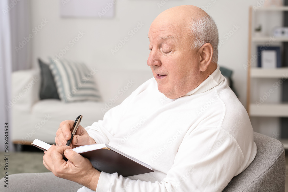 Portrait of elderly man writing in notebook at home Portrait of elderly man writing in notebook at home