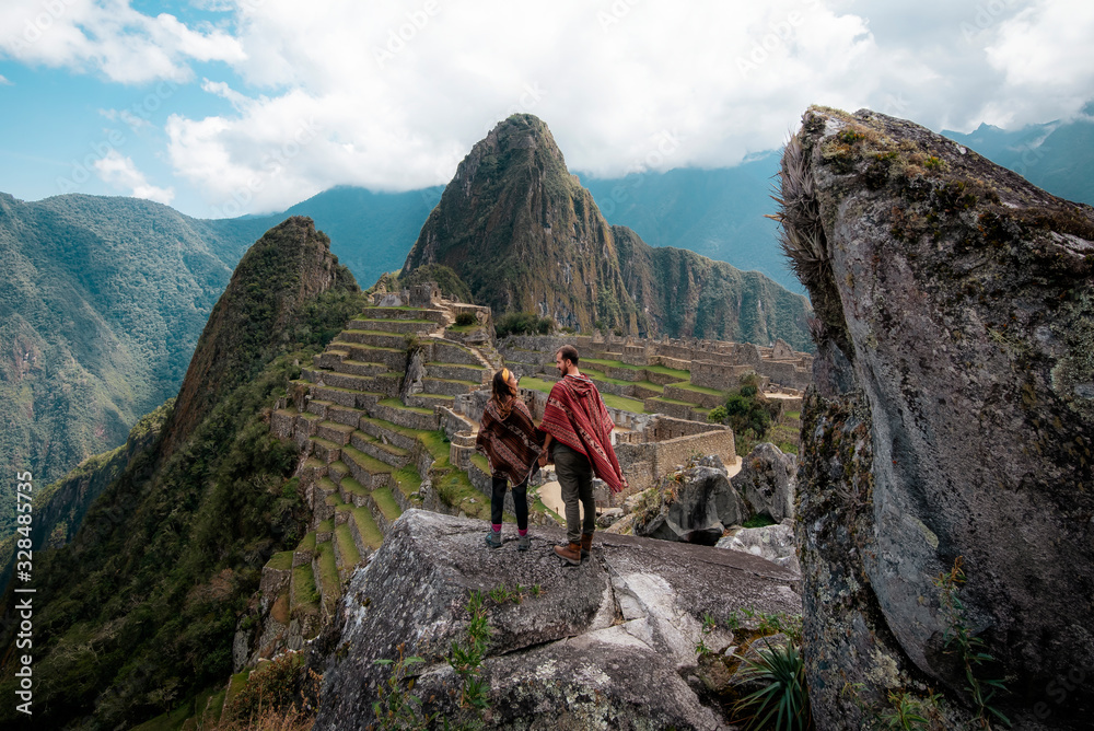 Couple dressed in ponchos watching the ruins of Machu Picchu - obrazy, fototapety, plakaty 