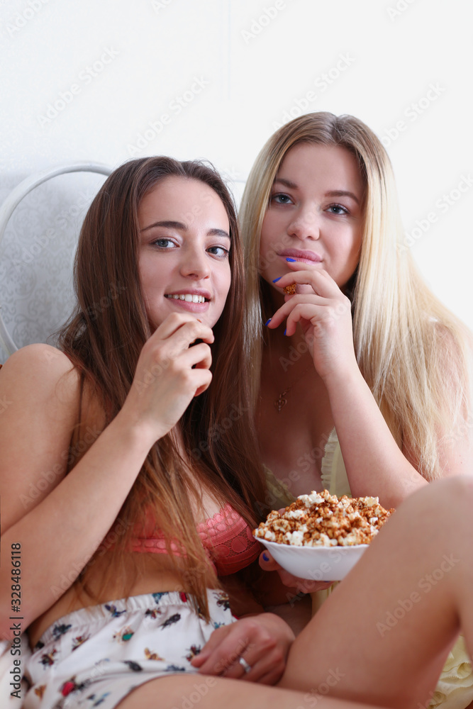 Two happy smiling girlfriends eat popcorn in bed watching TV show early morning holding remote control in hand portrait. Joy cozy tenderness lifestyle football match happiness or tv series concept Two happy smiling girlfriends eat popcorn in bed watching TV show early morning holding remote control in hand portrait. Joy cozy tenderness lifestyle football match happiness or tv series concept