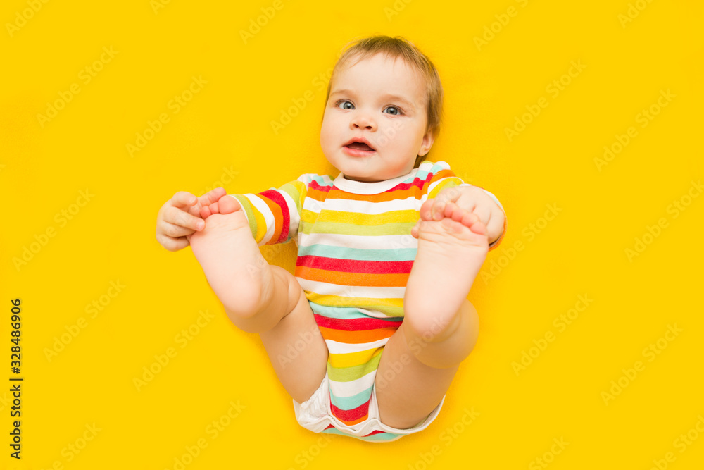 Baby plays with his feet on yellow background Baby plays with his feet on yellow background