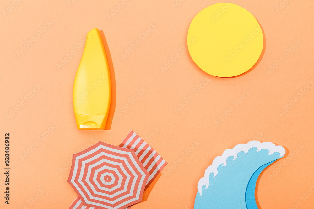 Top view of paper cut beach with tube of sunscreen on orange