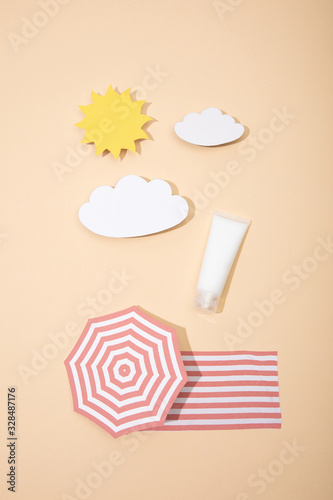 Top view of paper cut sun, clouds, beach umbrella and blanket with tube of sunscreen on beige photo