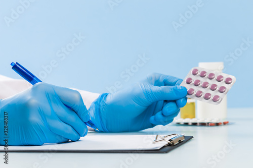 Doctor's hands in blue medical gloves write a prescription and hold a blister of pills on a blue background. concept of medicine, cardiology