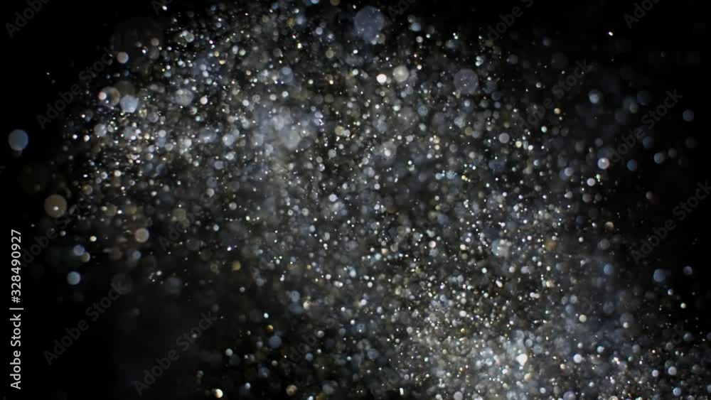 Gold and silver glitter flying after being exploded, bright sparkles bouncing against camera flying and falling down on black background. Top view close up macro slow motion
