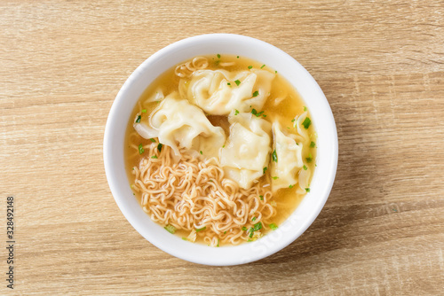 Instant noodles soup and wonton dumpling stuffed with minced pork in a bowl on wooden background, Asian food, Top view