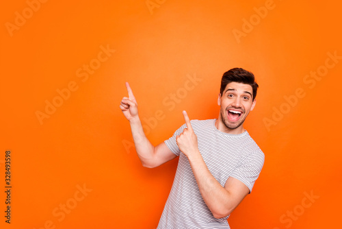 Photo of attractive guy hold hands fingers direct up empty space excited good mood sales person wear striped t-shirt isolated bright orange color background