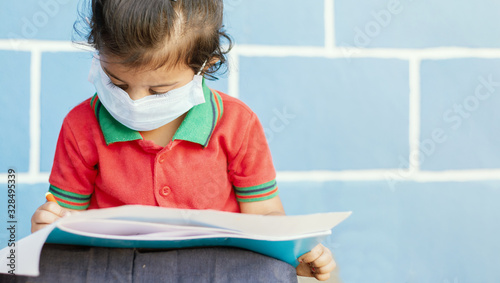 Covid 19 or Coronavirus and Air pollution pm2.5 concept - Little girl wearing medical mask and busy in writing at school - showing Wuhan covid-19 or sars cov 19 outbreak or epidemic of virus.