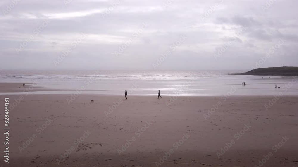 People walking their dogs on a sandy beach in winter. The tide is out and It's a cloudy, windy day on Barry Island, Wales, UK. People walking their dogs on a sandy beach in winter. The tide is out and It's a cloudy, windy day on Barry Island, Wales, UK.