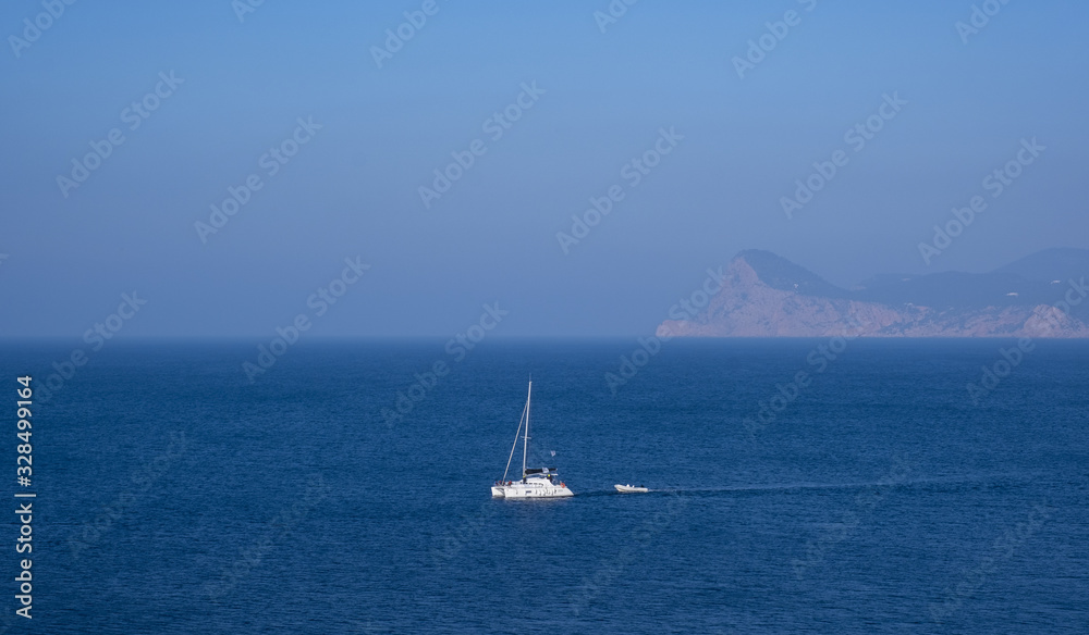 Sailboat sailing through the blue sea, views from Cap de la Bassa, Ibiza, Balearic Islands