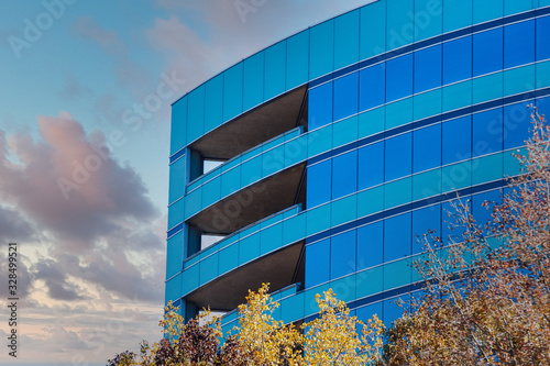 A curved, green and blue office building in autumn