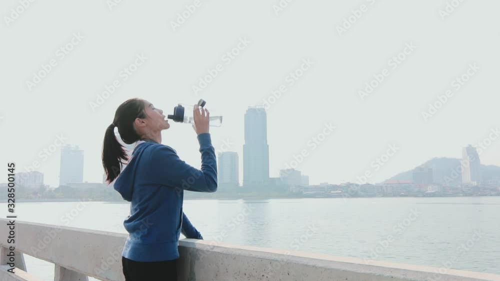 Attractive sporty girl happily drinking water after workout beside the sea and the city background. Attractive sporty girl happily drinking water after workout beside the sea and the city background.