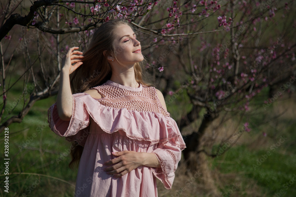 Beautiful blonde woman in pink dress walks through the flowering garden Beautiful blonde woman in pink dress walks through the flowering garden