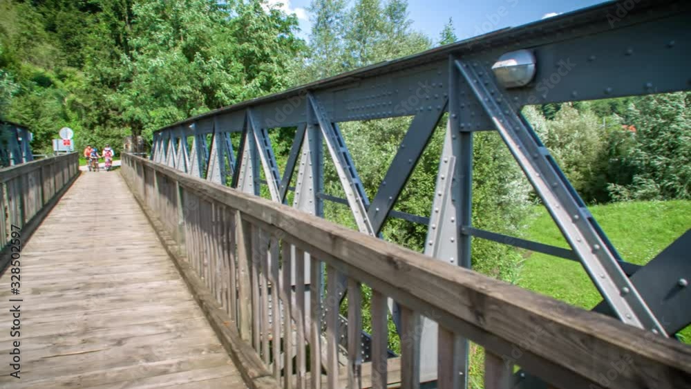 Pan overview of the metal and wooden bridge in a close-up view. Cyclists entering the bridge in the backdrop. Pan overview of the metal and wooden bridge in a close-up view. Cyclists entering the bridge in the backdrop.