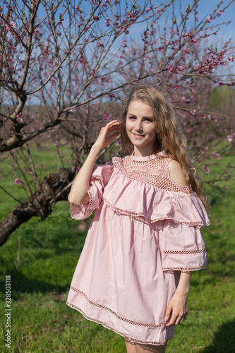 Beautiful blonde woman in pink dress walks through the flowering garden