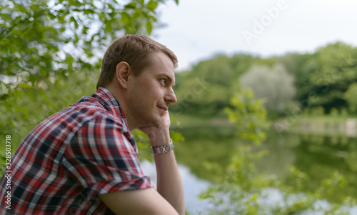 Young pensive man looks at the river. Unity with nature.