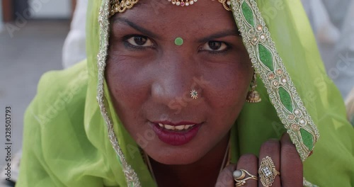 Close-up of an attractive confident positive happy Indian woman wearing green salwar kameez, traditional dress with head covered in sheer fabric, looks smiles at camera smiles- handheld slow motion photo