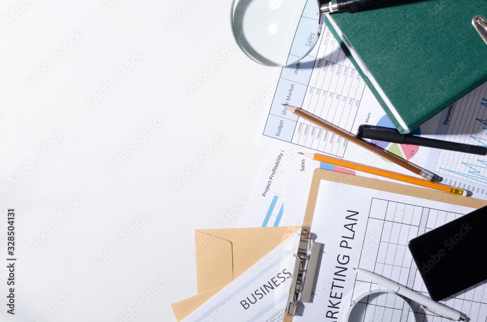 Top view of office desk and business documets on it.Marketing plan, business documents,magnifying glass, smartphone on the white table.Empty space for text.Concept of business work and searching facts