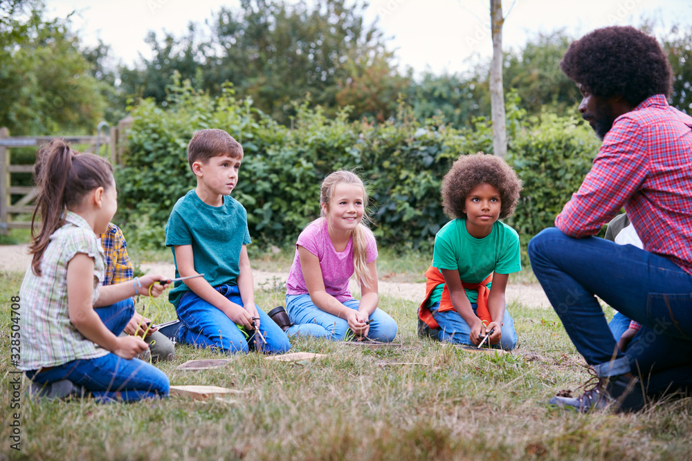 Fototapeta premium Team Leader Showing Group Of Children On Outdoor Camping Trip How To Make Fire