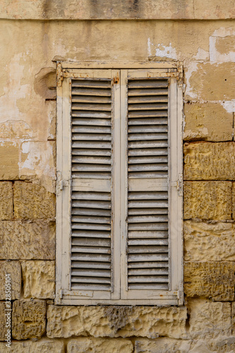 Old wooden shutter in a house wall built of Malta stone blocks