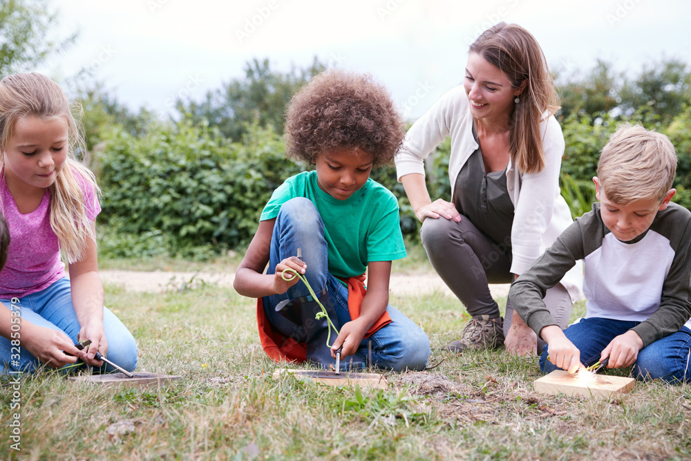 Female Team Leader Showing Group Of Children On Outdoor Camping Trip How To Make Fire Female Team Leader Showing Group Of Children On Outdoor Camping Trip How To Make Fire