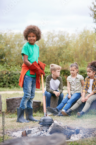 Group Of Children On Outdoor Activity Camping Trip Cooking Over Camp Fire Together