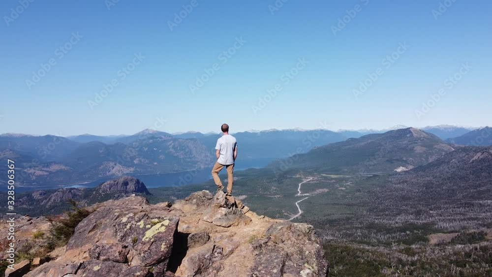 Aerial drone scene turning over point of interest on young athletic man over mountain summit watching wide landscape of lakes and mountain chains. San Martin de los Andes, Neuquen, Argentina Aerial drone scene turning over point of interest on young athletic man over mountain summit watching wide landscape of lakes and mountain chains. San Martin de los Andes, Neuquen, Argentina