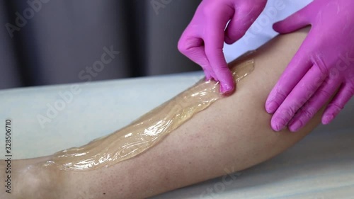 azulene depilation. wax hair removal, shugaring. concept of smooth skin without hair. azulene color. the master puts azulene on the girls legs photo