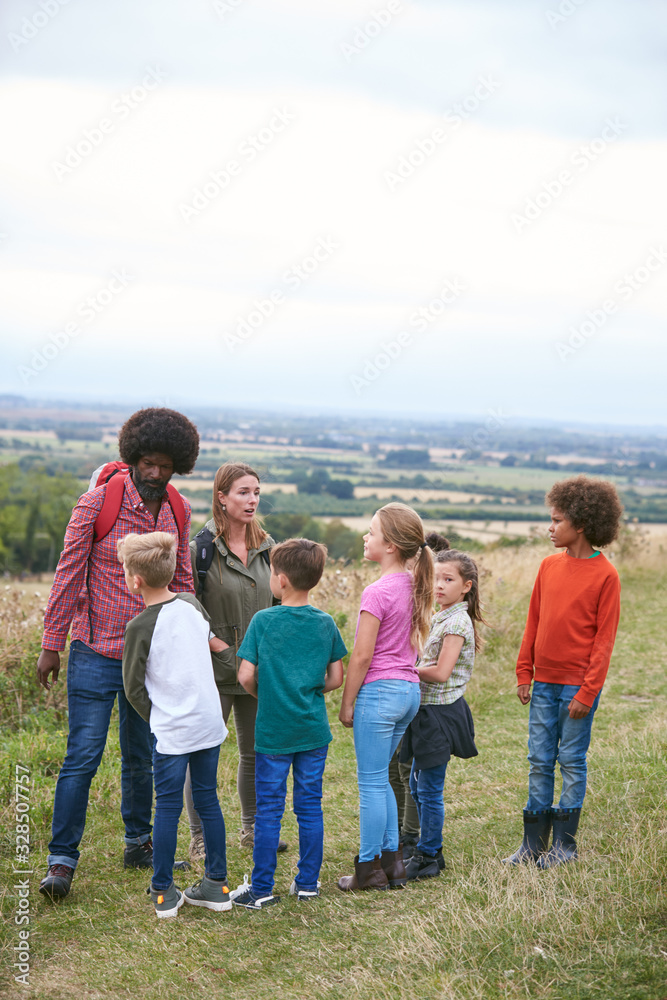 Adult Team Leaders With Group Of Children At Outdoor Activity Camp Walking Through Countryside Adult Team Leaders With Group Of Children At Outdoor Activity Camp Walking Through Countryside
